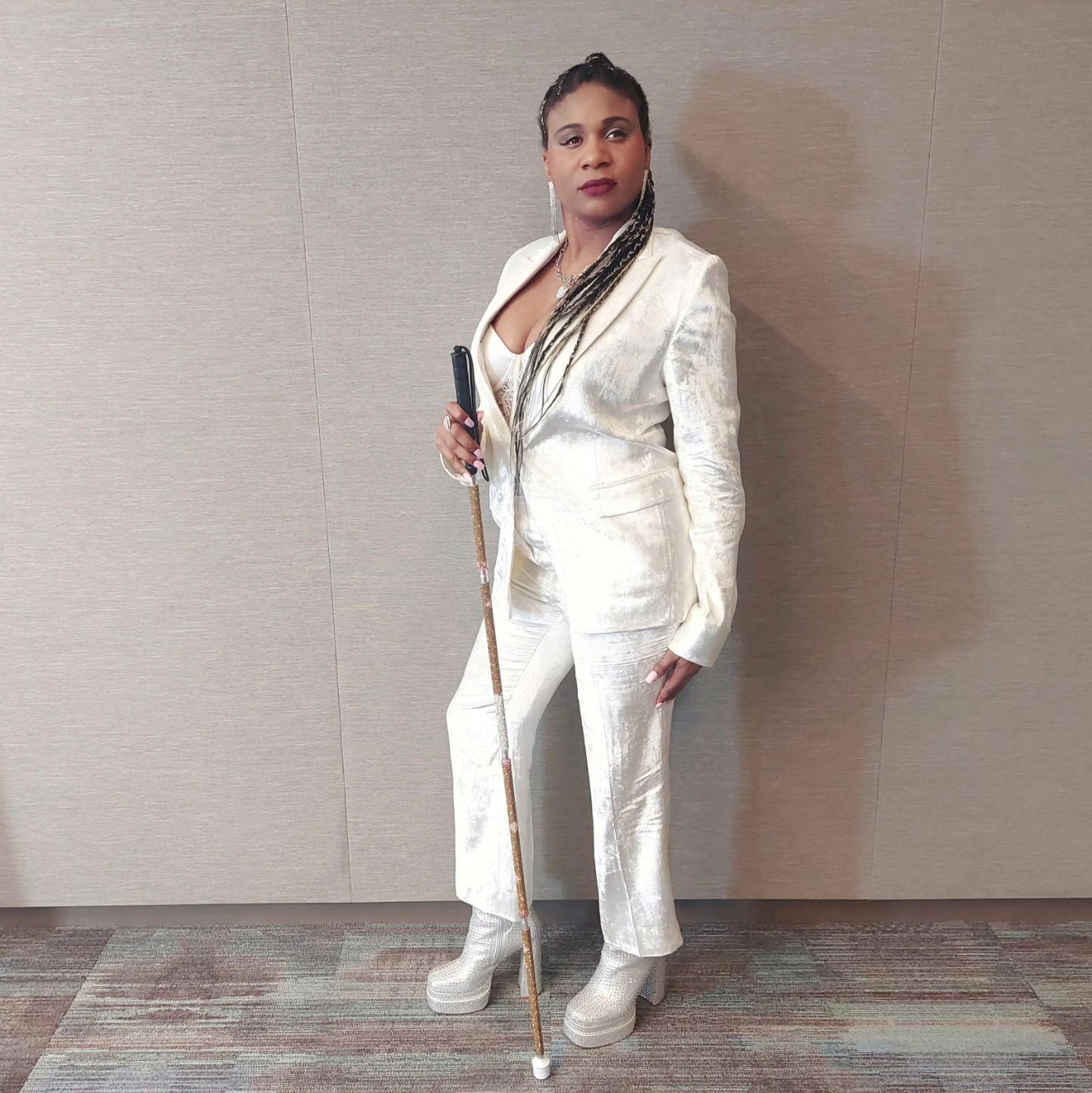 Lachi, a black woman with cornrows, poses with a gold and white glam cane and an all white pantsuit