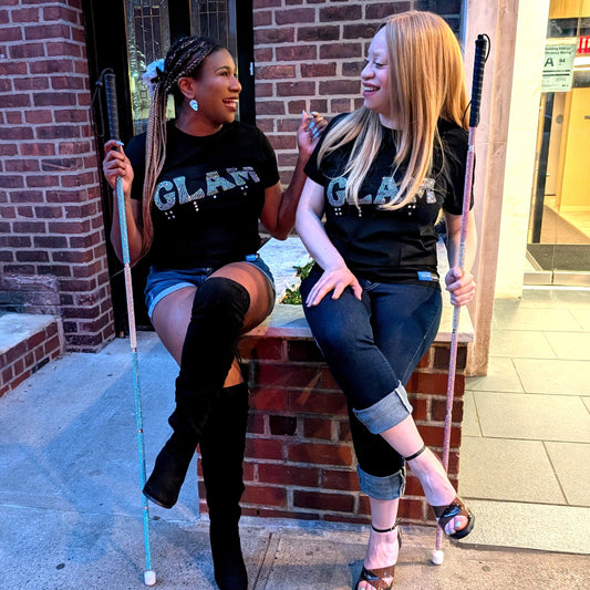 Two women sitting on a brick ledge wearing GLAM t-shirts, holding canes.
