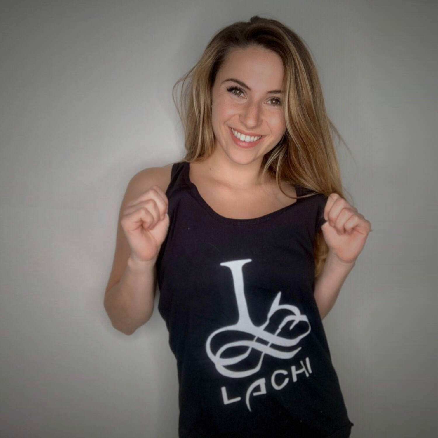A white woman shows off her black shirt with the word "Lachi" and a stylized letter L emblazoned on the front