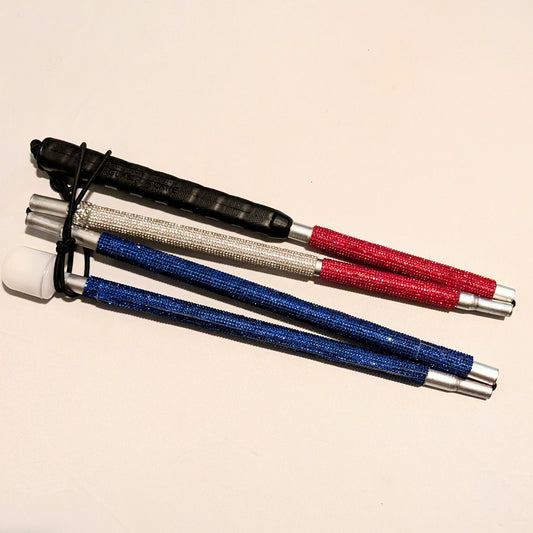 A folded blind cane, covered in rhinestones that  are ruby red at the top, silvery white in the middle, and blue towards the bottom.