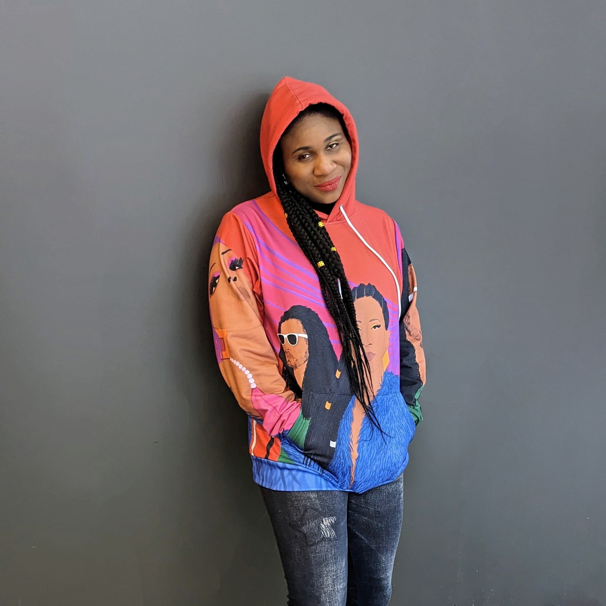 Lachi, a black woman with cornrows, poses wearing a colorful sweater featuring the album art for her single Black Girl Cornrows which has drawn profiles of Lachi and the other artists over an orange background