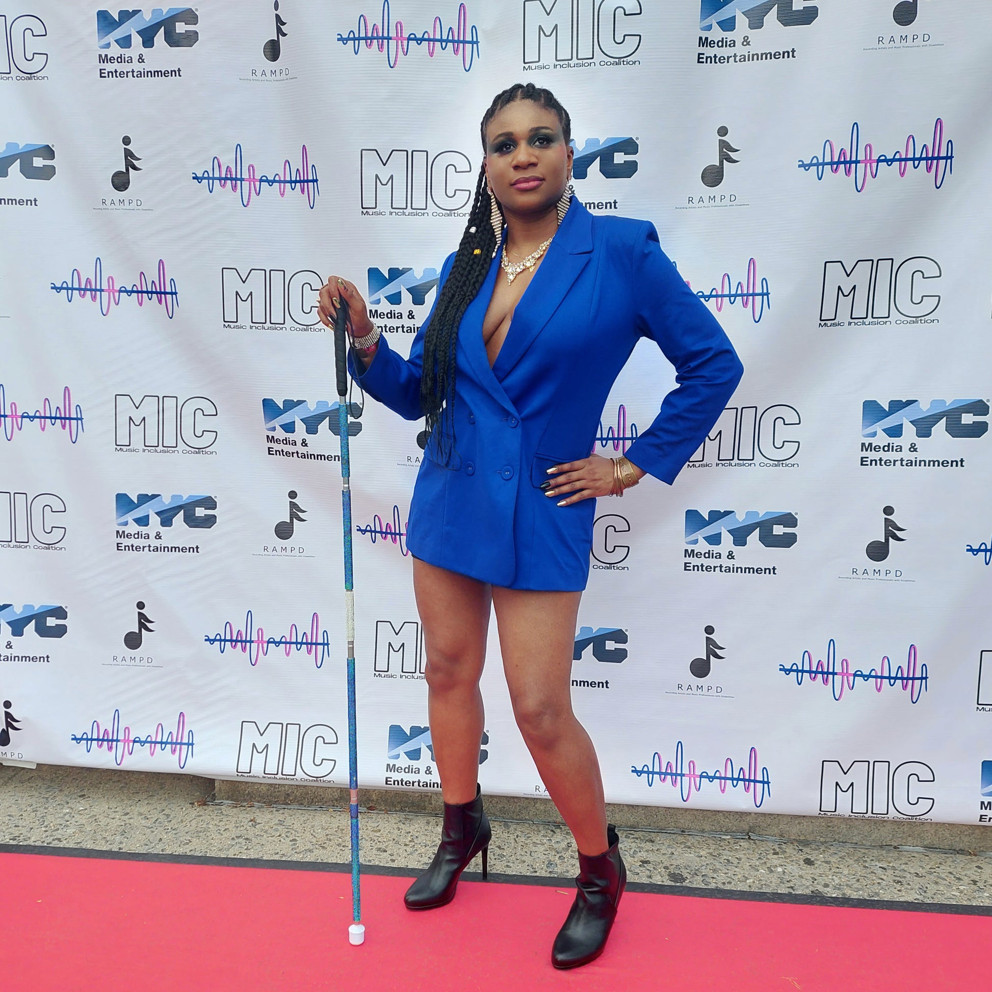 Lachi, a black woman with cornrows, poses in a blue dress with a blue and white rhinestone glam cane